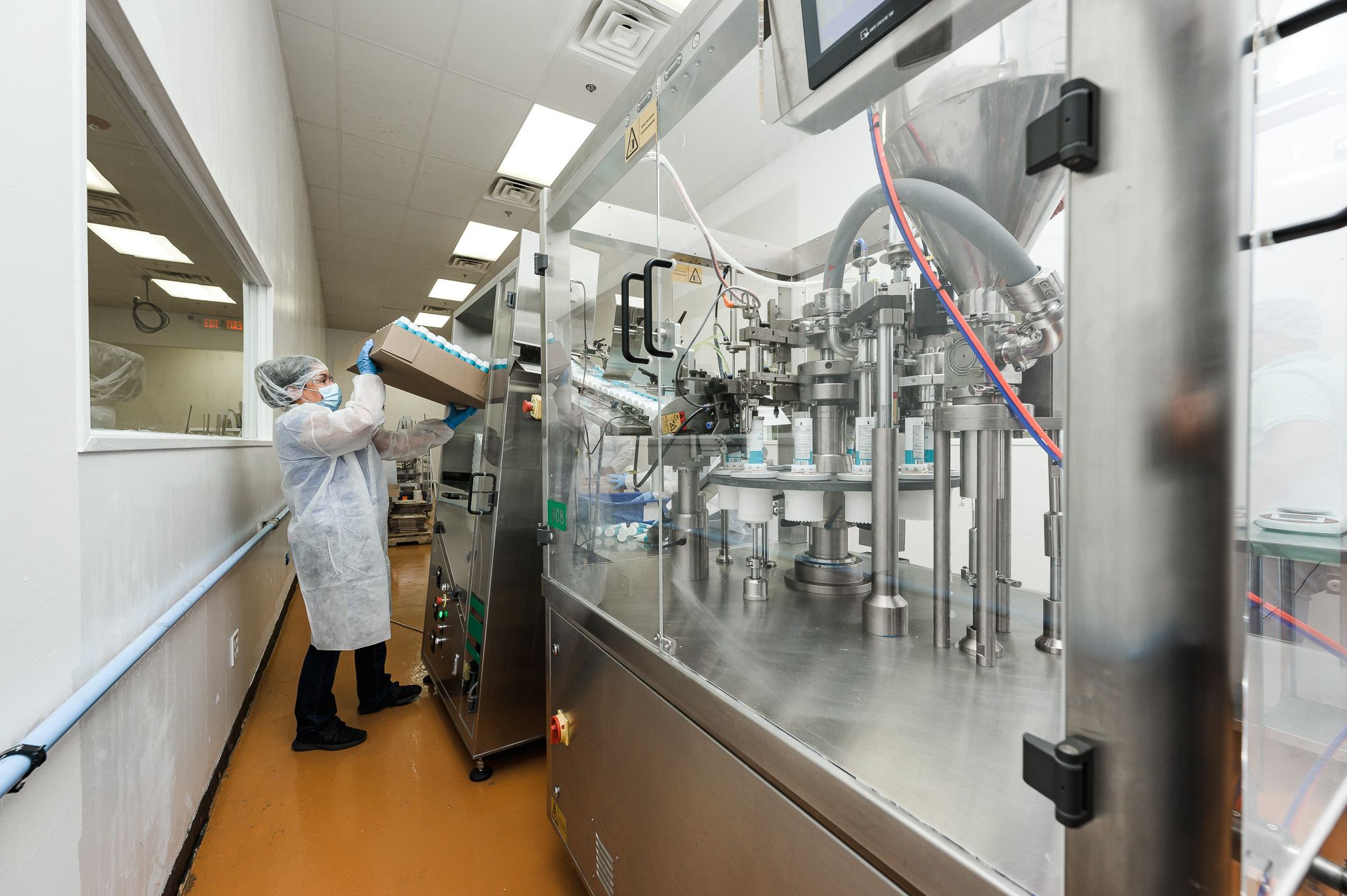 Operator in PPE loading bottles into an automated filling machine