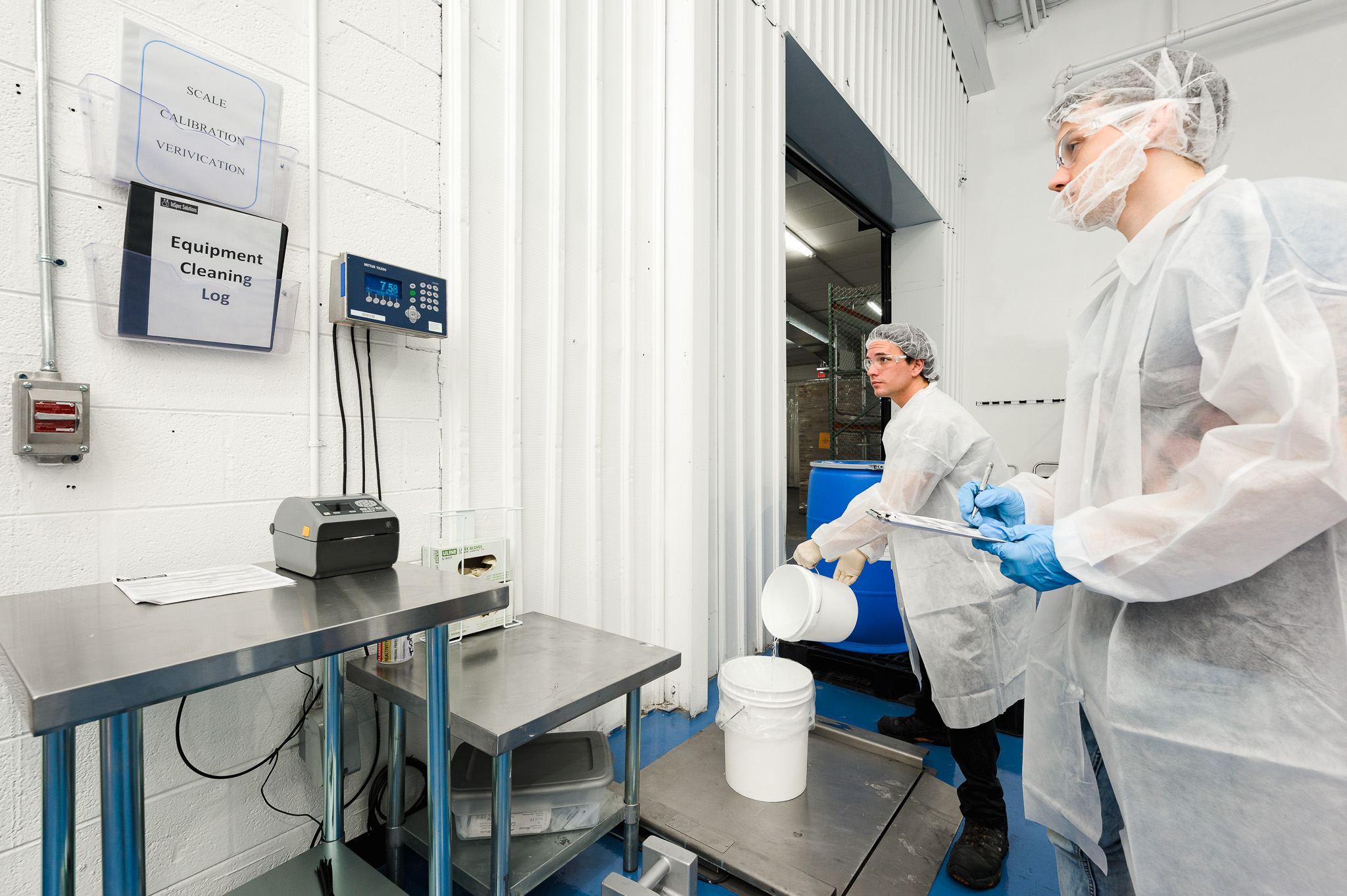 Technicians dispensing raw material at a weigh station with calibration and cleaning logs