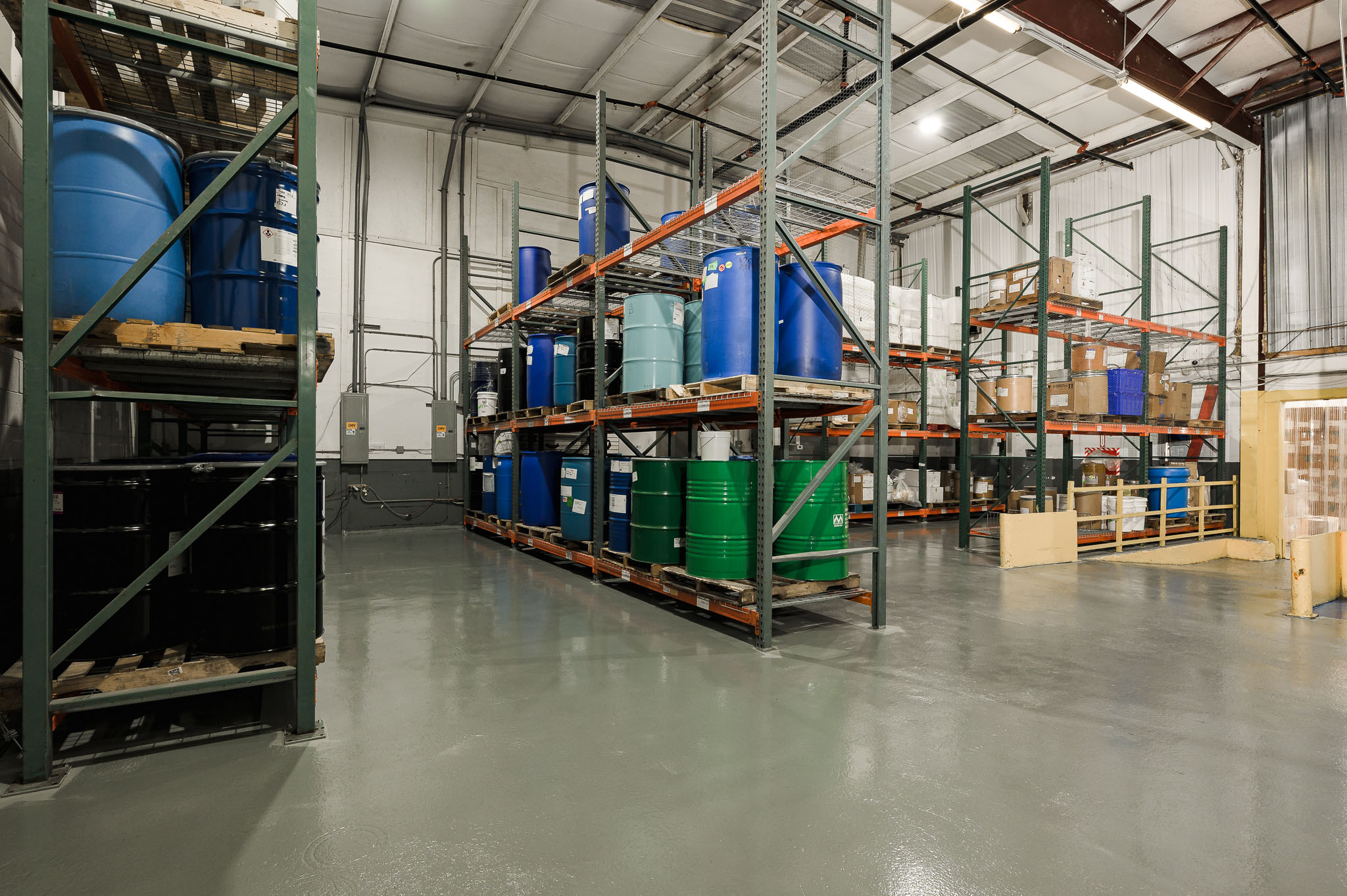 Warehouse racks storing labeled chemical drums for raw materials